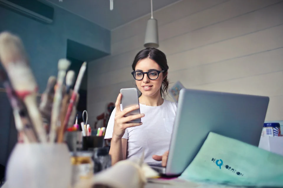 Woman working on laptop, looking at phone